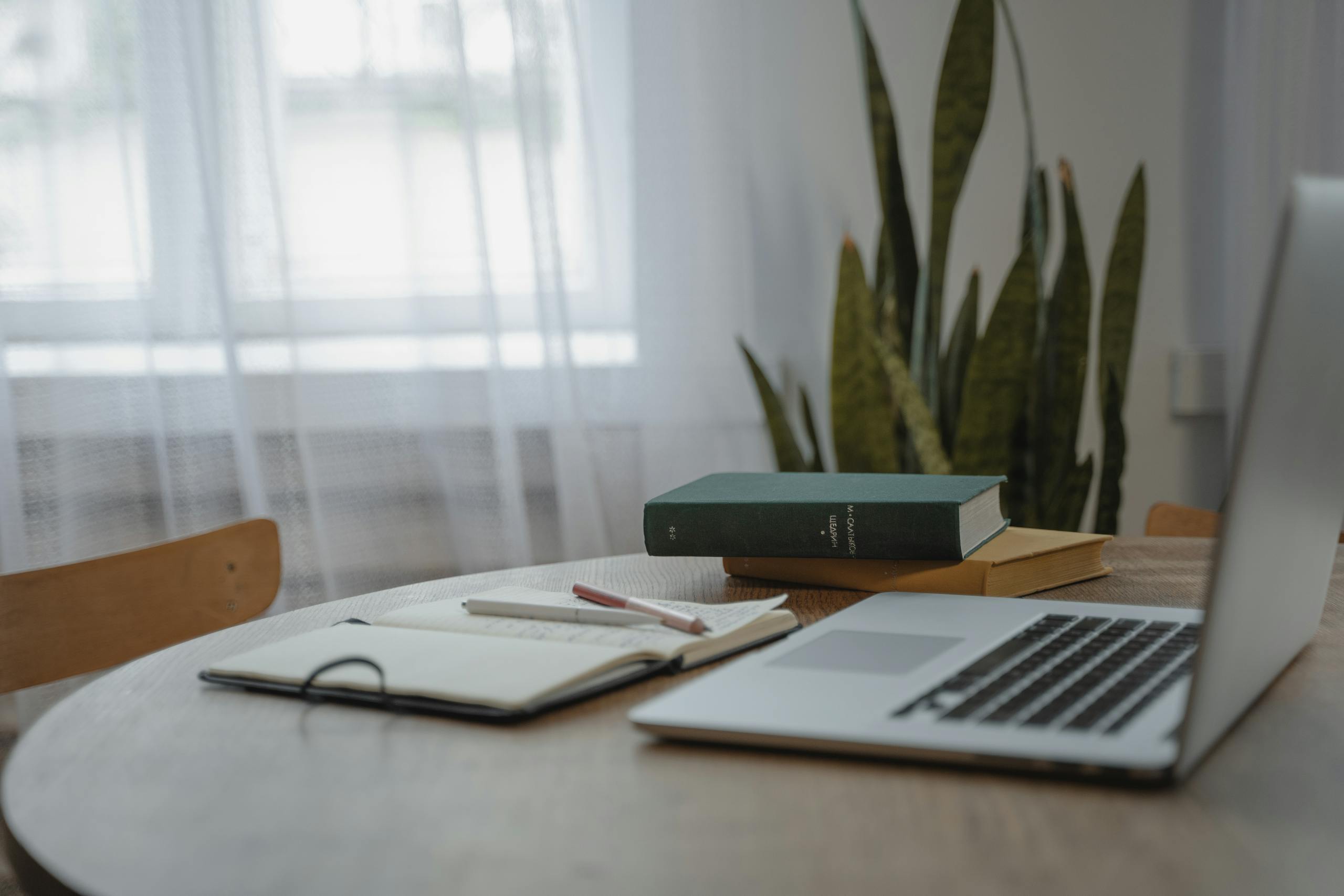 A tranquil indoor workspace featuring a laptop, books, and a notebook for studying or remote work.